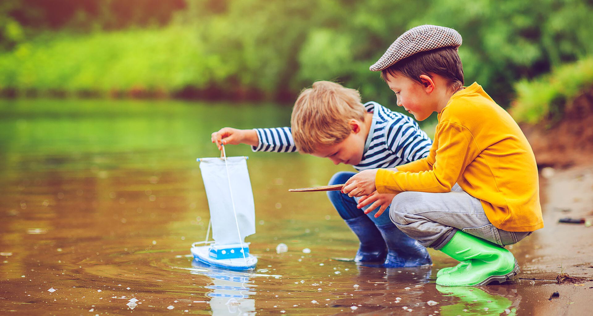 Zwei Kinder mit Spielzeugschiff am Ufer